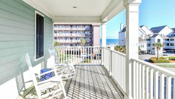 A wooden deck with white railings, a rocking chair, and a view of a multi-story building with balconies and a beach in the background. - 2nd Row 4 BR Beach House with a Shared Pool! - Chubby's Anchor (Surfside Beach)