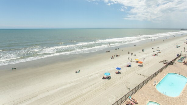 A beach with a swimming pool, umbrellas, and lounge chairs.