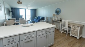 A modern kitchen with a large island, grey cabinetry, and a dining area with a blue sofa and chairs.