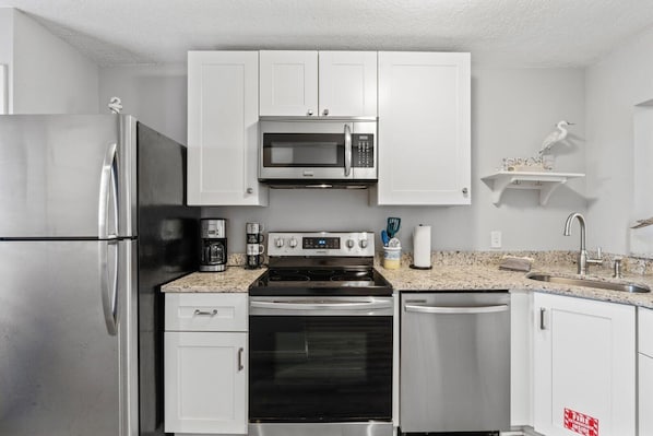 A modern kitchen with stainless steel appliances, white cabinets, and granite countertops. - Blessed By The Sea Crescent Beach Activities 2 Bedroom Home (St. Augustine)
