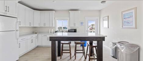Una cocina moderna con armarios blancos, una isla de madera oscura y vistas al exterior.