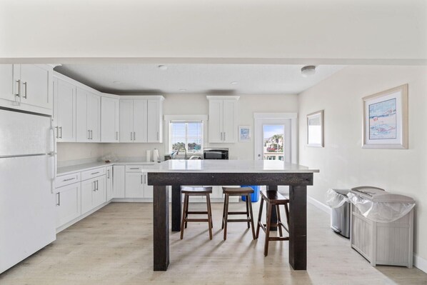 A modern kitchen with white cabinets, a dark wooden island, and a view of the outside.
