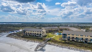 Ein Strandhotel mit mehreren Gebäuden, einem Schwimmbad und einer Promenade, die zum Strand führt.