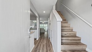 Ein modernes Interieur mit einer Holztreppe, weißen Wänden und einem durchgehenden Durchgang erkennbaren Küchenbereich.