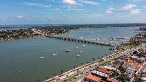 An aerial view of a coastal town with a marina, a bridge, and a road leading to a historic building. - Mystic Sands I Steps To Beach I Free Activities 2 Bedroom Condo (St. Augustine)