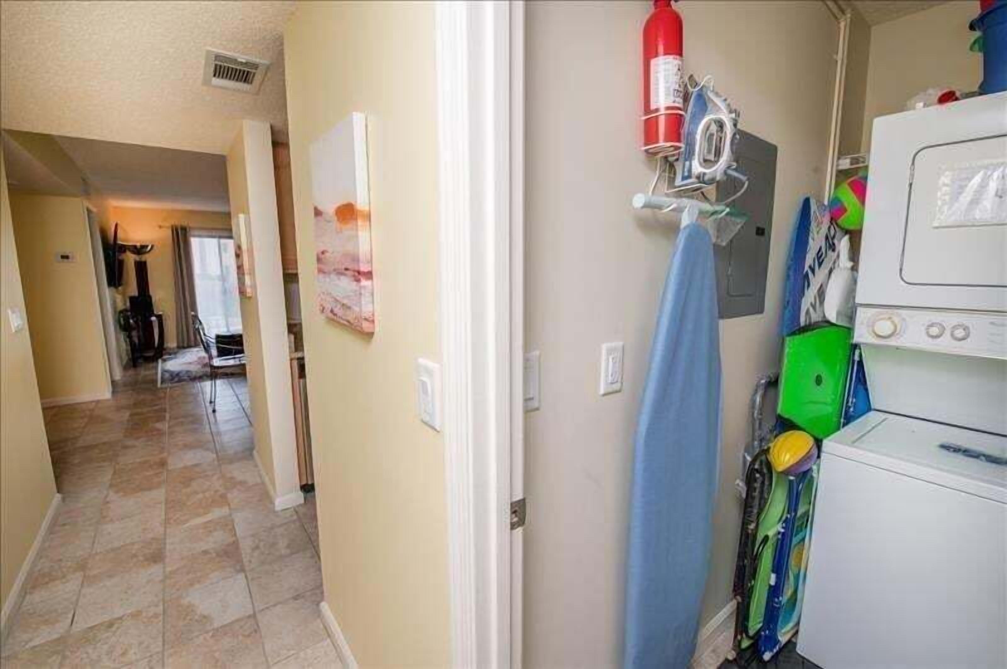 A hallway with a laundry area, including a washing machine, a fire extinguisher, and a towel rack.