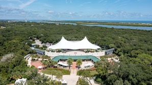 A large, white, tent-like structure with a green roof, surrounded by lush greenery and a body of water in the background. - Mystic Sands I Steps To Beach I Free Activities 2 Bedroom Condo (St. Augustine)