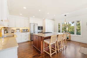 A modern kitchen with white cabinets, a wooden island, and a large window offering a view of greenery. - Stunning view in great Vanderhorst area location (Kiawah Island)