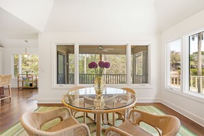 A round glass table with wicker chairs, a vase with flowers, and large windows with a view of trees. - Stunning view in great Vanderhorst area location (Kiawah Island)