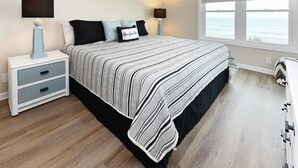 A bedroom with a bed, two bedside tables, a nightstand, a window with a view of the ocean, and a view of the beach. - Oceanfront 3 BR Condo with a Shared Pool! Surf Harbor 203 (Surfside Beach)