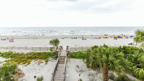 A beach with a wooden boardwalk leading to the shore, palm trees, and umbrellas. - Oceanfront 3 BR Condo with a Shared Pool! Surf Harbor 203 (Surfside Beach)
