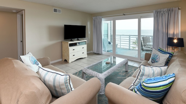A living room with a television, two sofas, a coffee table, and a view of the ocean through a sliding glass door. - Oceanfront 3 BR Condo with a Shared Pool! Surf Harbor 203 (Surfside Beach)