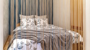 Una cama bien hecha con un edredón estampado y almohadas, un cabecero de madera y una cortina con rayas verticales.
