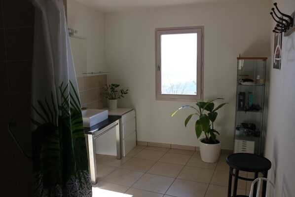 Una cocina pequeña y limpia con ventana, una planta en maceta y un taburete.