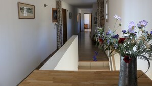 En gang med trægulv, en metalvase med blomster og en trappe.