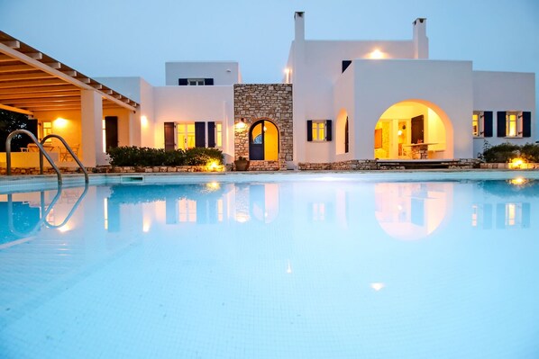 A swimming pool with a stone archway and a covered seating area. - Villa Haroula, Private Pool Villa with Panoramic Aegean Sea and Sunset View. (Paros)