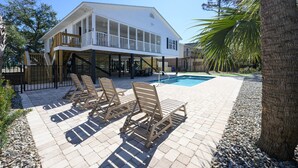 Una casa de dos pisos con balcón, piscina y mobiliario de exterior.