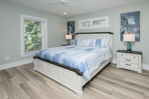 Une chambre à coucher comprenant un lit, des tables de chevet, un ventilateur de plafond et des œuvres d’art accrochées aux murs.