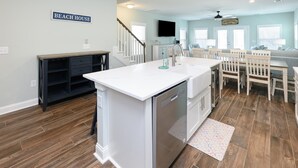 Een keuken met een wit aanrecht, een houten vloer en een bordje met de tekst 'BEACH HOUSE'.