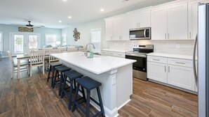 Een moderne keuken met witte kastjes, een groot kookeiland met barstoelen, en een roestvrijstalen koelkast.