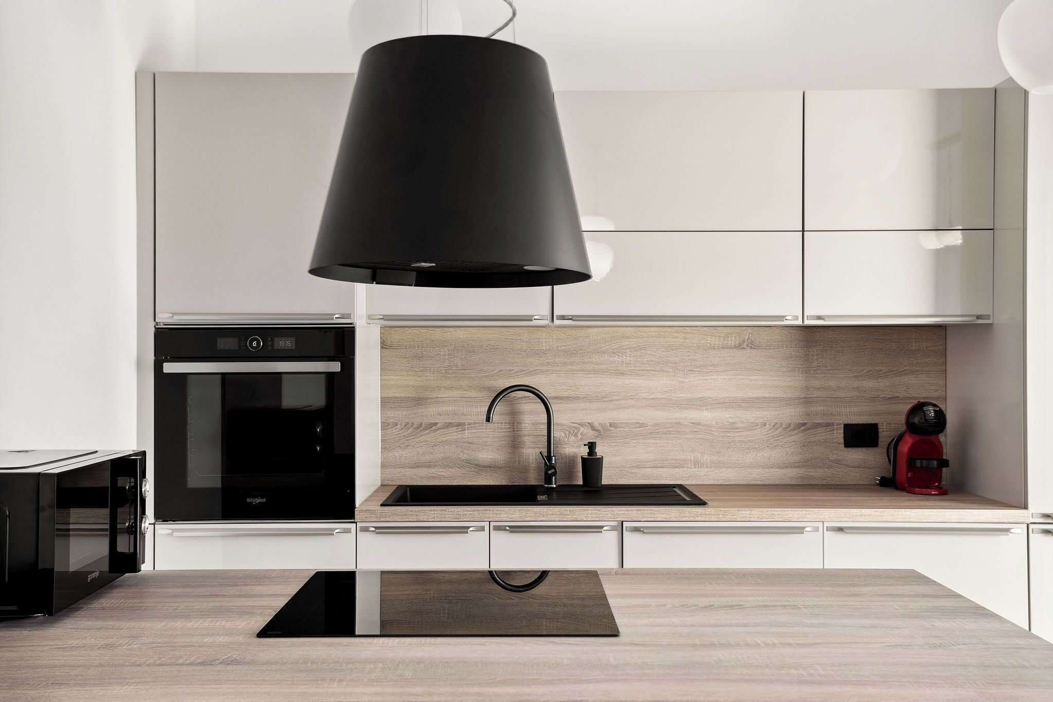 A modern kitchen with a black pendant light, a built-in oven, and a wooden backsplash.