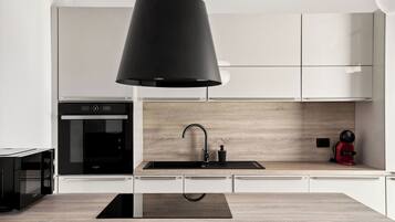 A modern kitchen with a black pendant light, a built-in oven, and a wooden backsplash.