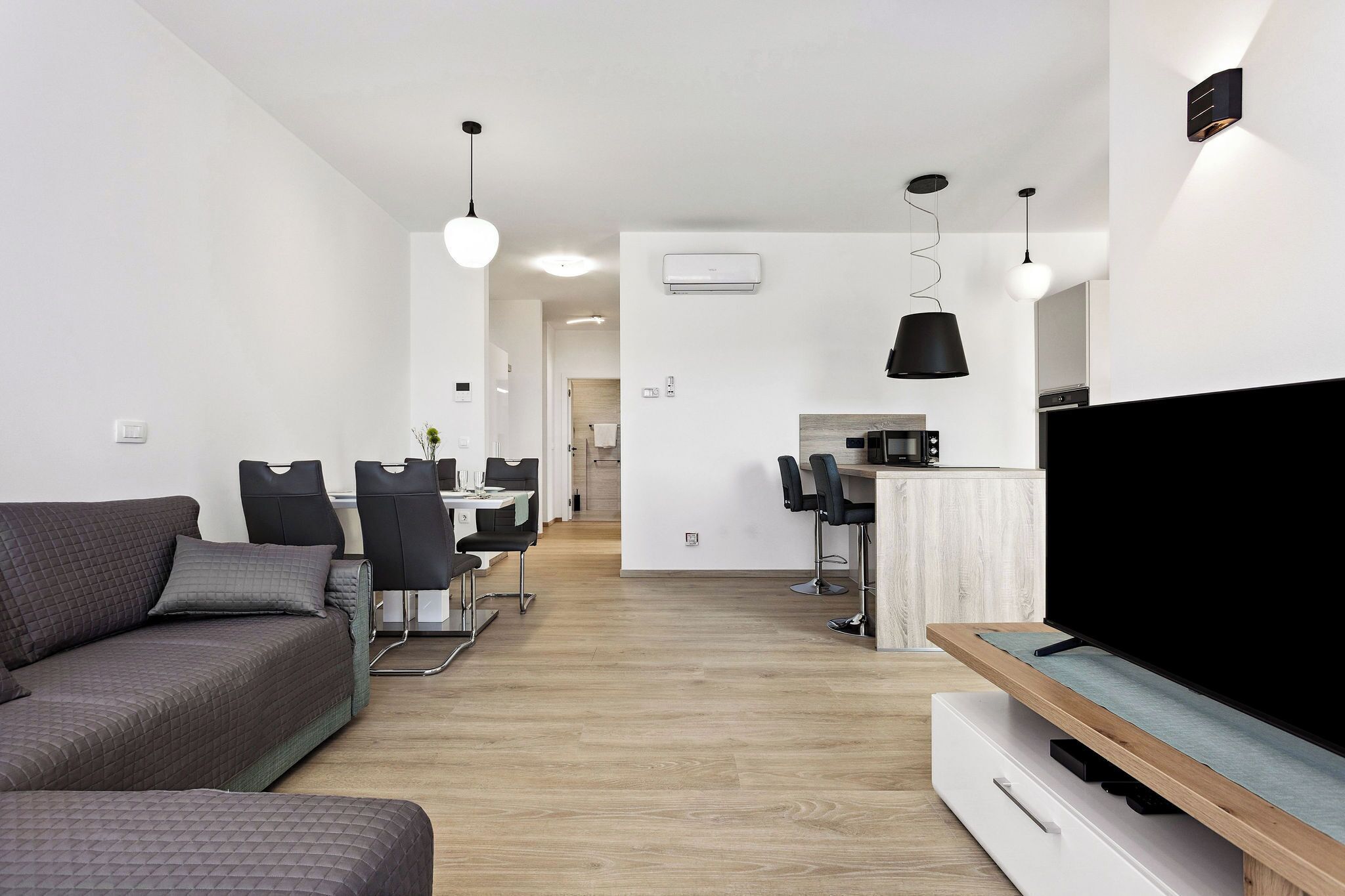 Ein modernes Wohnzimmer mit einer Couch, einem Fernseher und einem Essbereich mit Stühlen und einem Tisch.
