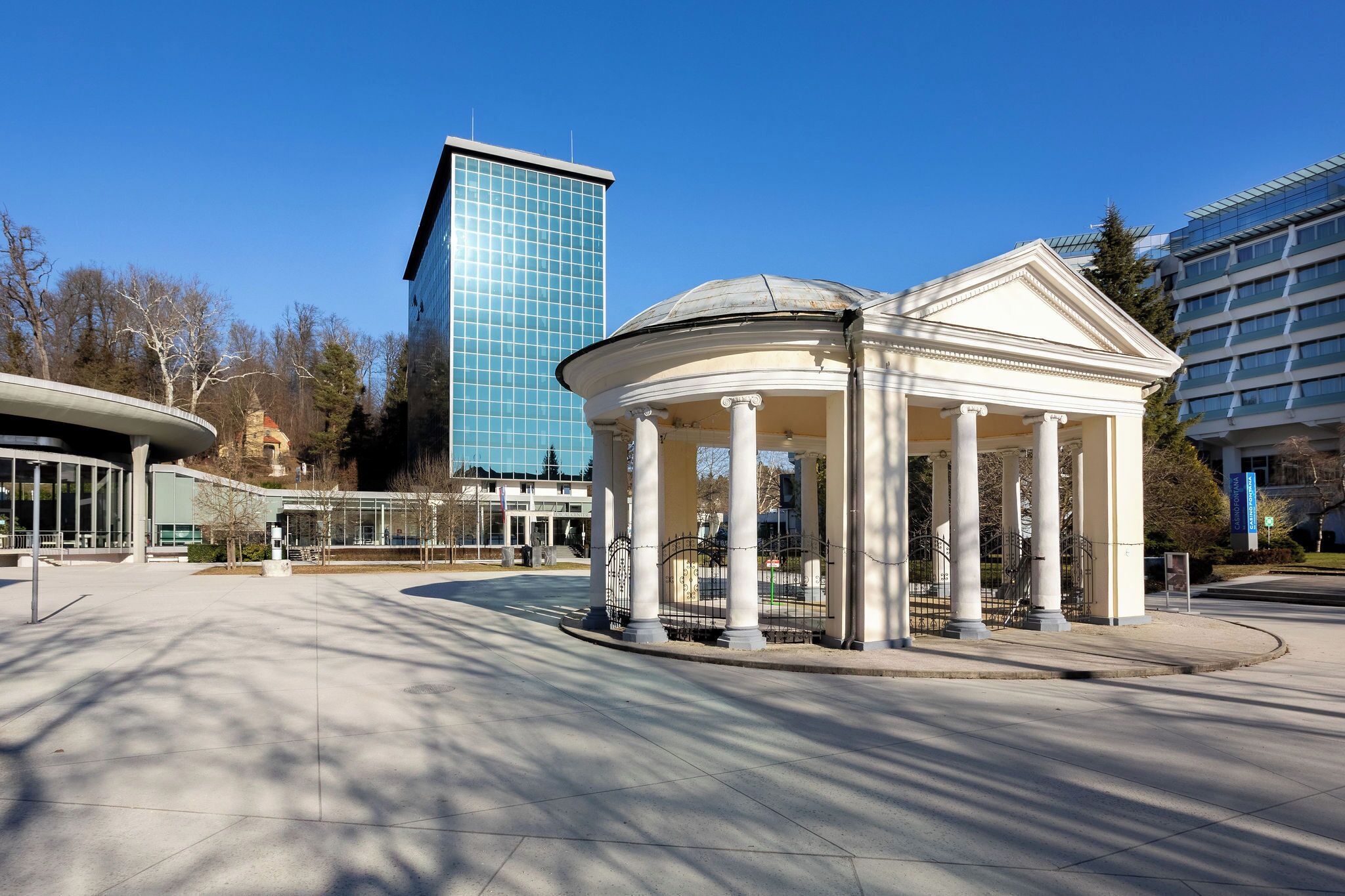 A pavilion with columns, a modern building in the background, and a clear sky.