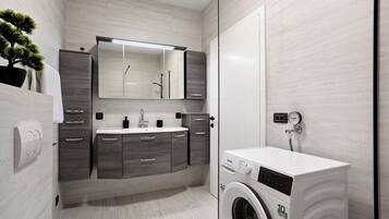 A modern bathroom with grey cabinetry, a built-in sink, a mirror, a washing machine, and a potted plant.
