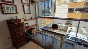 A balcony with a glass table and chairs, a wooden dresser, and framed artwork on the wall. - Ap Punta Cana em Balneário Camboriú - SC (Balneário Camboriú)