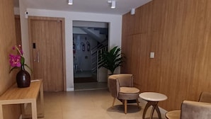 A modern lobby with wooden paneling, a reception desk, seating area, and a staircase leading to an upper floor. - Ap Punta Cana em Balneário Camboriú - SC (Balneário Camboriú)