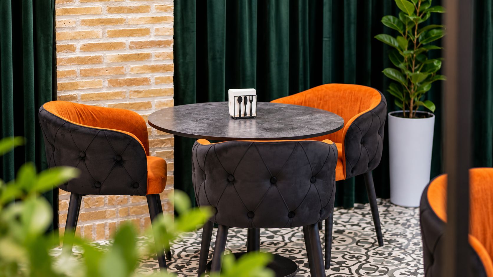 A round table with a black top, surrounded by four chairs with black and orange upholstery.