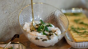 A clear glass bowl with a creamy substance and green leaves, placed on a wooden surface with a metal spoon. - Badyan Hotel (Bukhara)