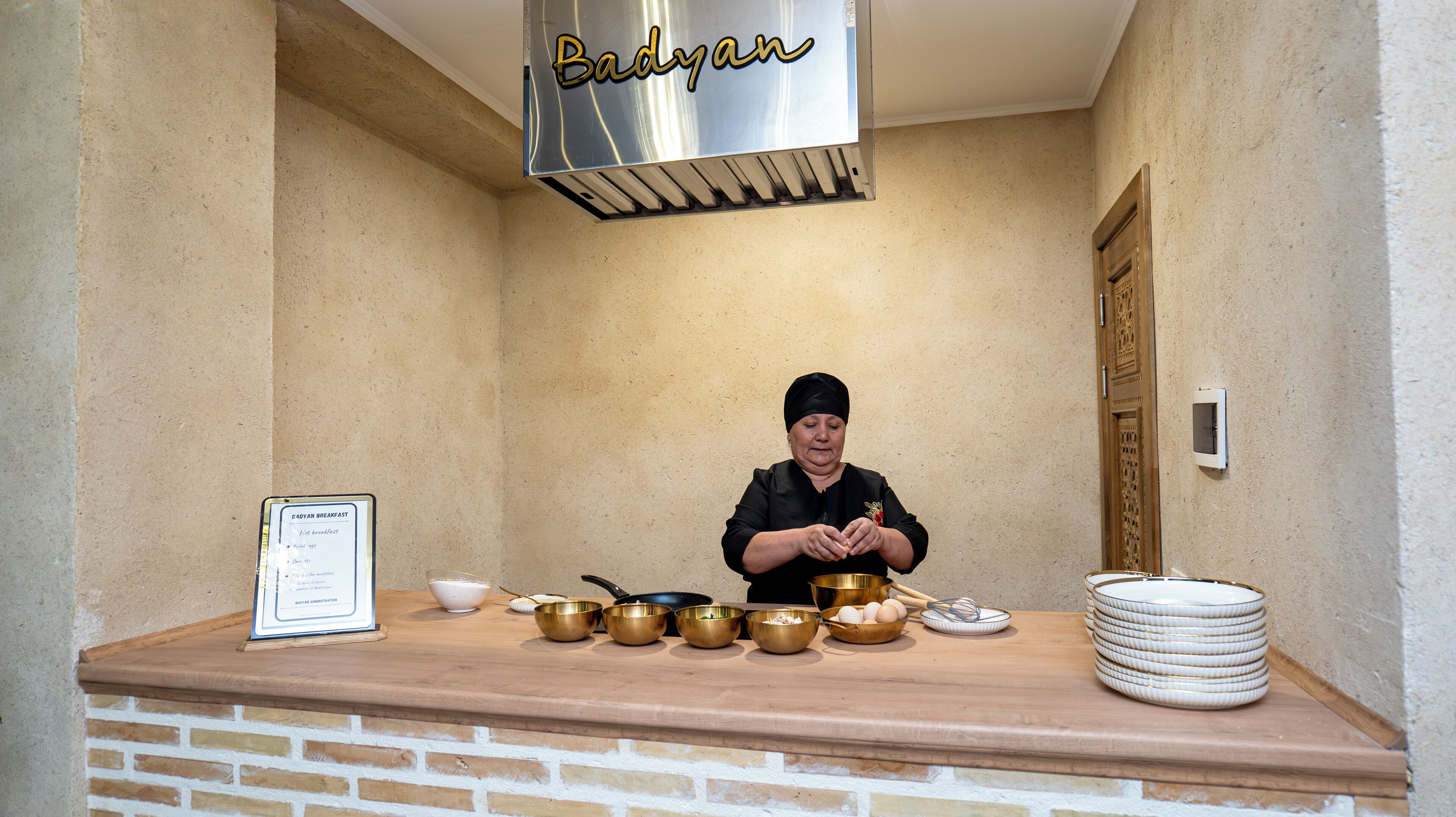 A chef preparing food in a kitchen with a sign reading "Badyan Breakfast".