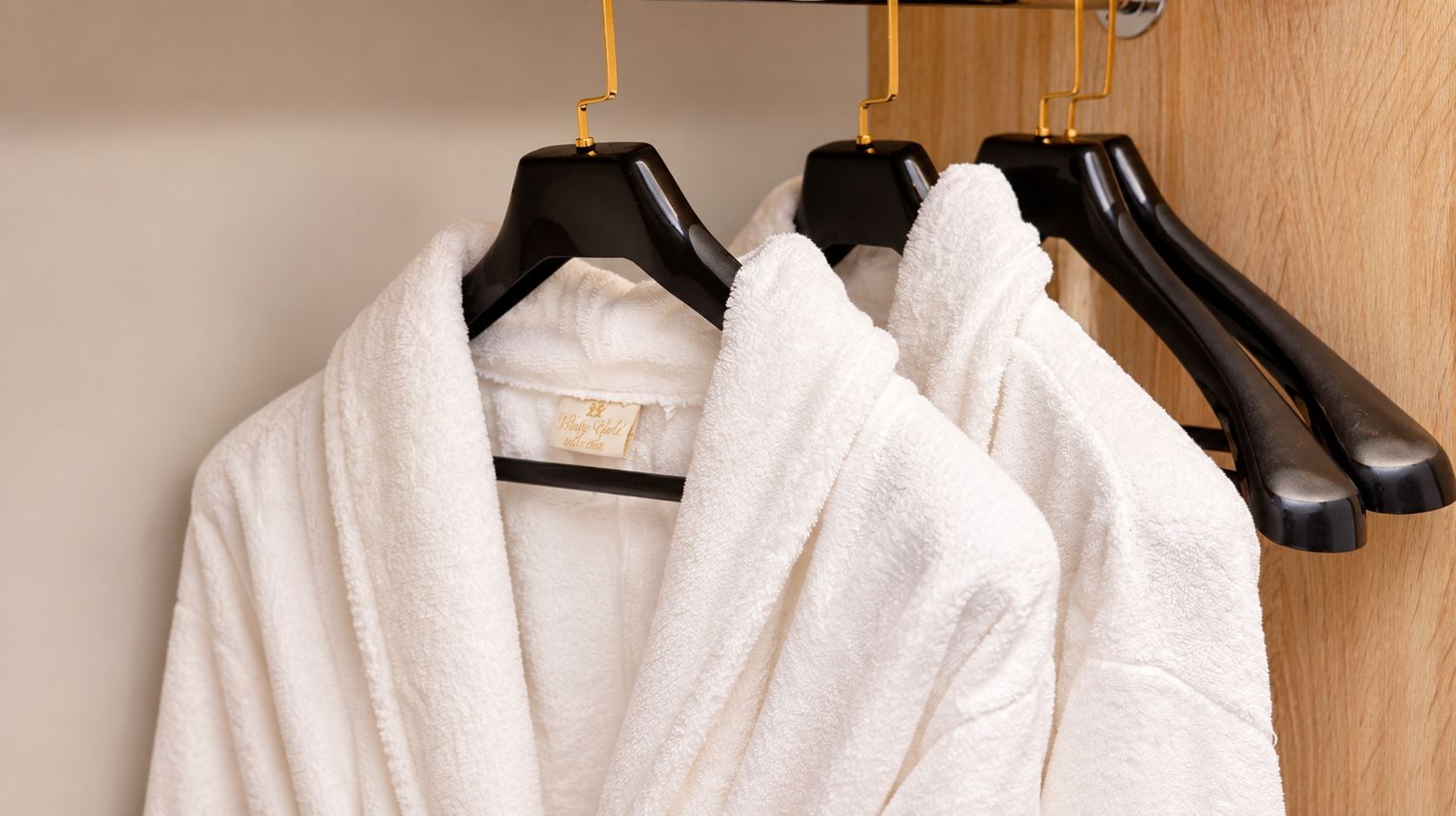 A white bathrobe hanging on a black hanger with a gold-colored hook.