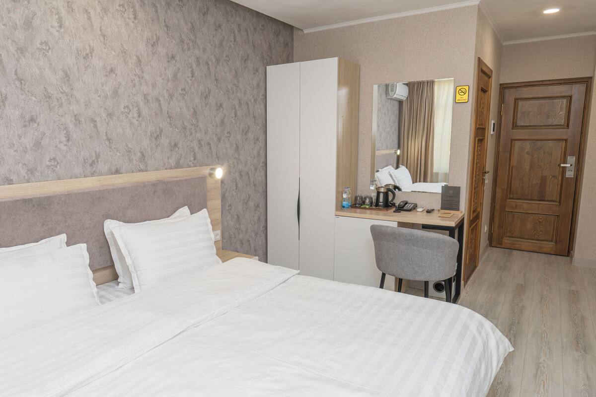 A hotel room with a bed, a desk, a chair, a wardrobe, and a mirror.