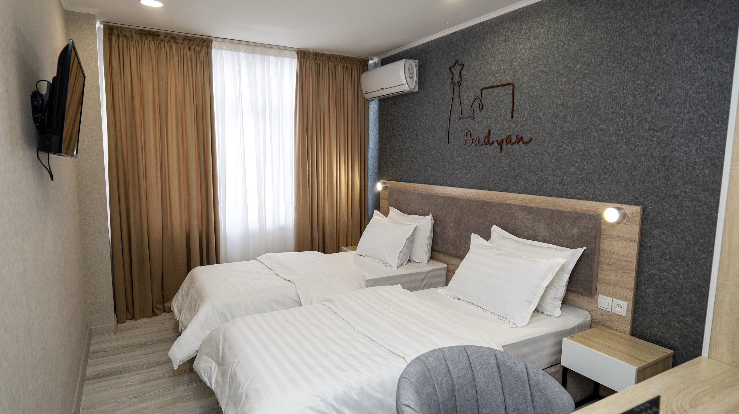 Habitación de hotel con dos camas, un escritorio, una silla, un televisor y aire acondicionado instalado en la pared.