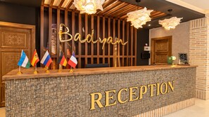 En receptionsdisk med en skylt som visar ”RECEPTION”, ett antal flaggor och en dekorativ vägg med en skylt som visar ”Baidyan”.