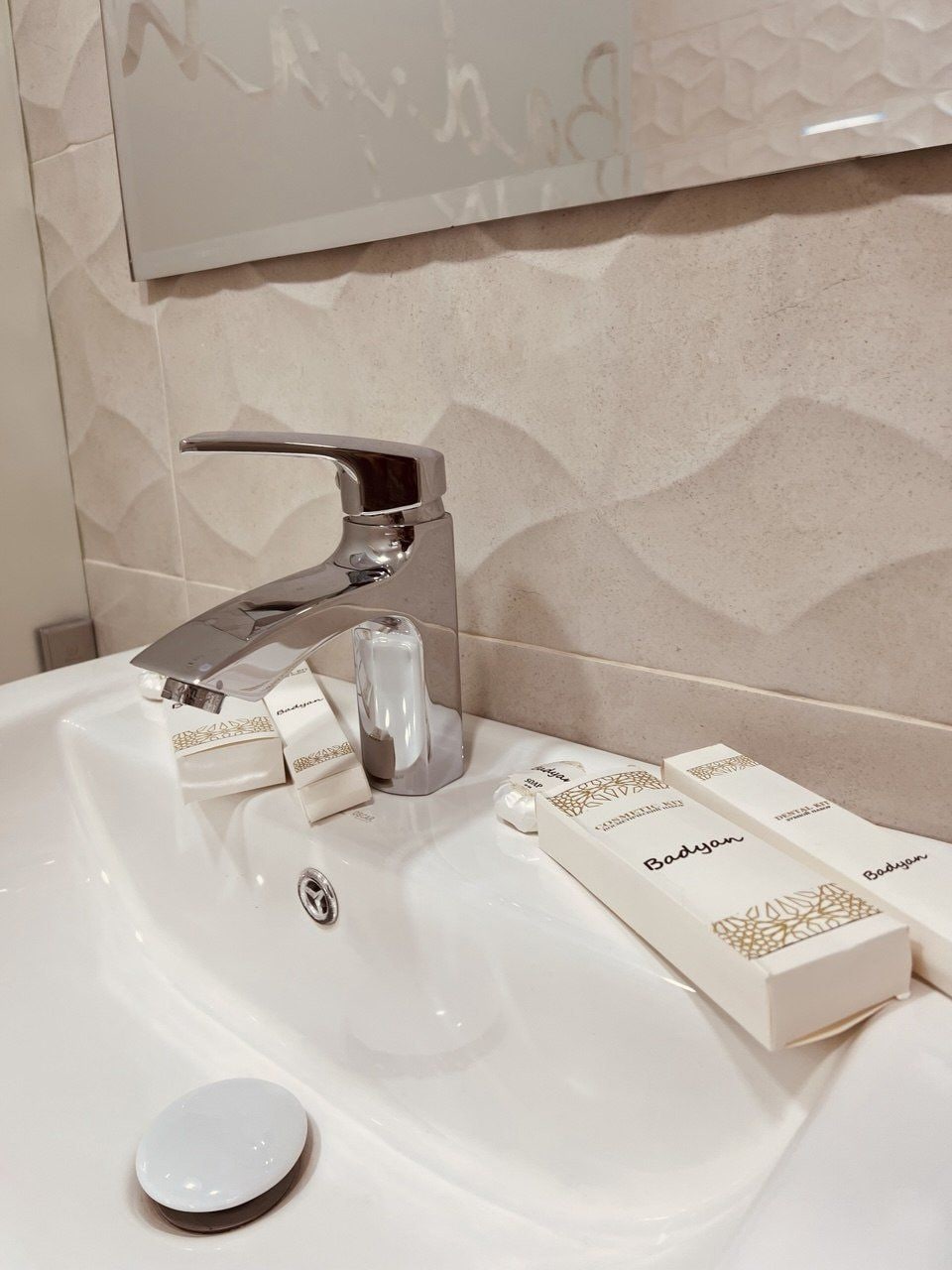 Un lavabo de salle de bain avec un robinet moderne, un distributeur de savon et quelques savons en barres posés sur le comptoir.