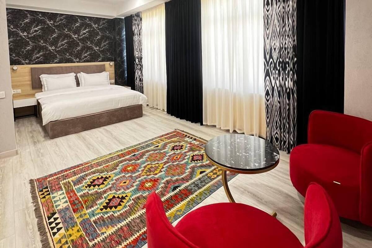 A modern hotel room with a bed, a red chair, a small table, and a patterned rug.