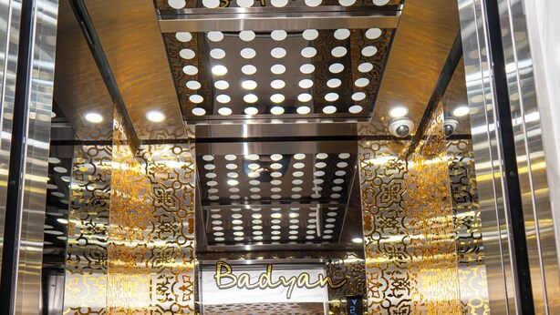 An interior view of a modern elevator with a metallic and patterned design, featuring a digital display and a sign reading "Badyan". - Badyan Hotel (Bukhara)
