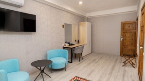 A modern room with a TV, a desk, two chairs, a small table, and a wooden door. - Badyan Hotel (Bukhara)