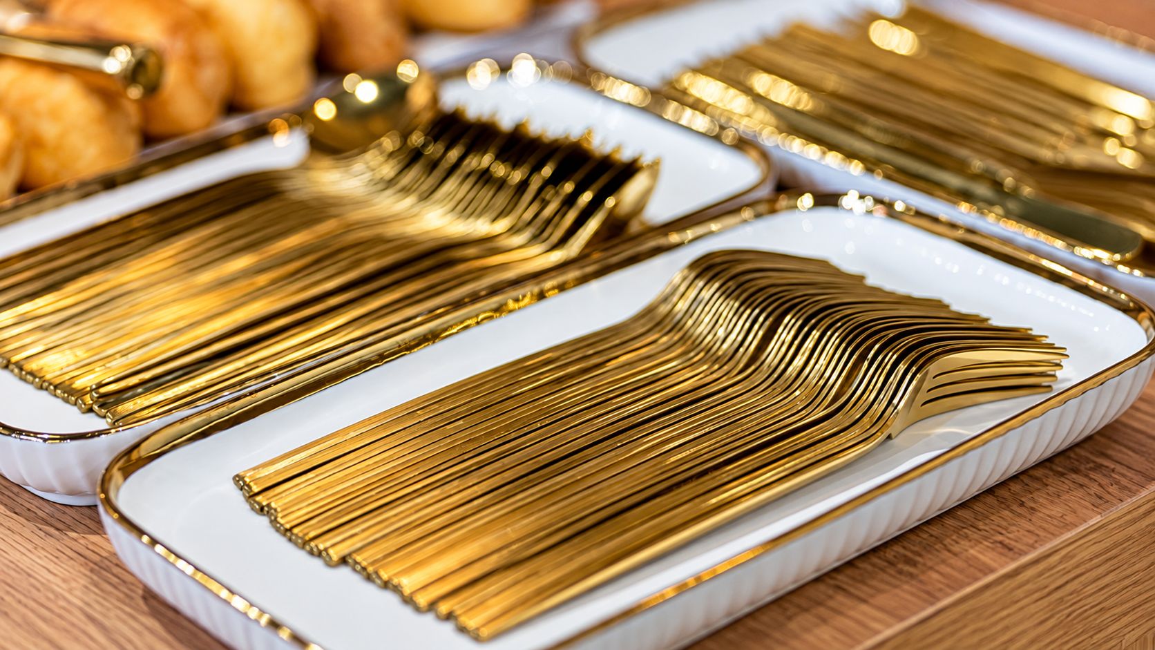A close-up of a white rectangular plate with a gold rim, containing a stack of gold-colored utensils.