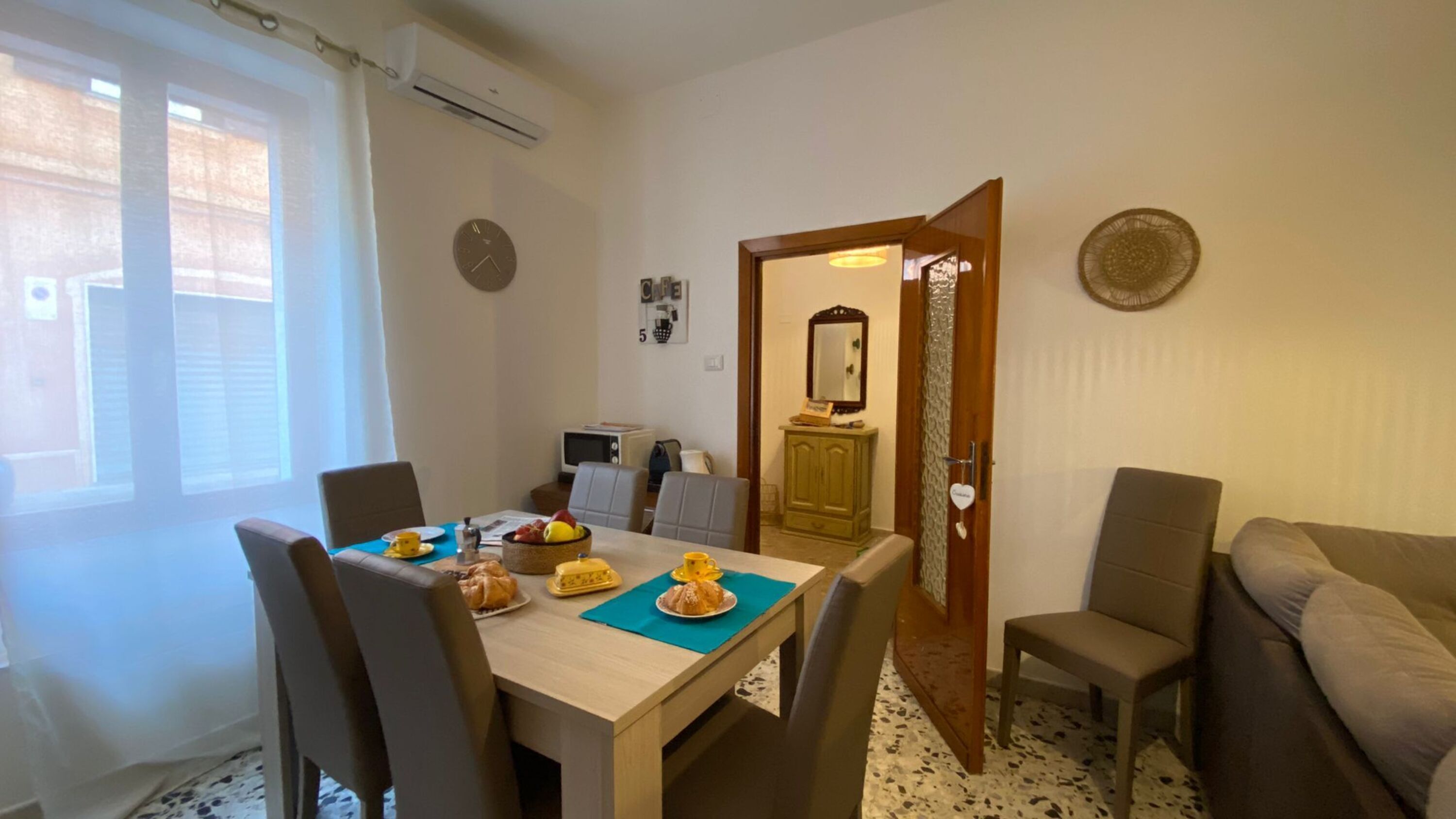 Een eetgedeelte met een tafel voor twee personen, een bank en een deur naar een andere kamer.