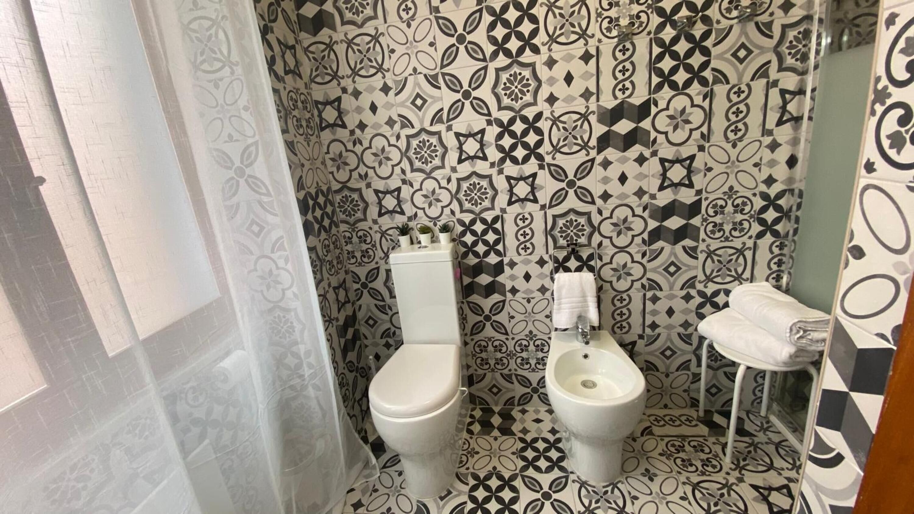 A bathroom with a patterned tile wall, a toilet, a bidet, and a small sink.