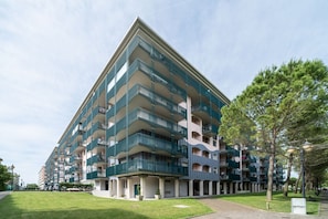 A multi-story residential building with balconies, a grassy courtyard, and a clear sky.