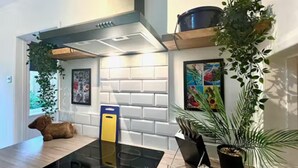 A modern kitchen with a glass stovetop, white brick backsplash, and a hanging plant. - Woodcrest Retreat Sleeps 4 With Garden (Reigate)