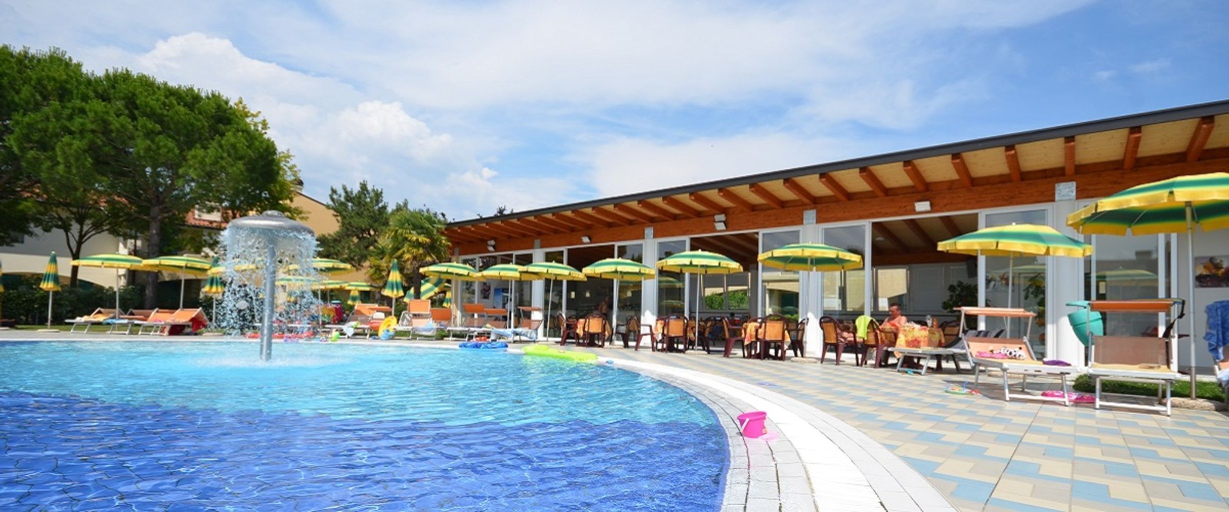 A pool area with lounge chairs and umbrellas, a covered seating area, and a clear sky.