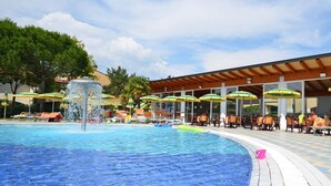 Ein Poolbereich mit Liegestühlen und Sonnenschirmen, eine überdachte Sitzecke und ein klarer Himmel.