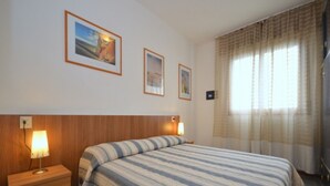 Una habitación de hotel con una cama, una mesita de noche, una lámpara y dos cuadros en la pared.